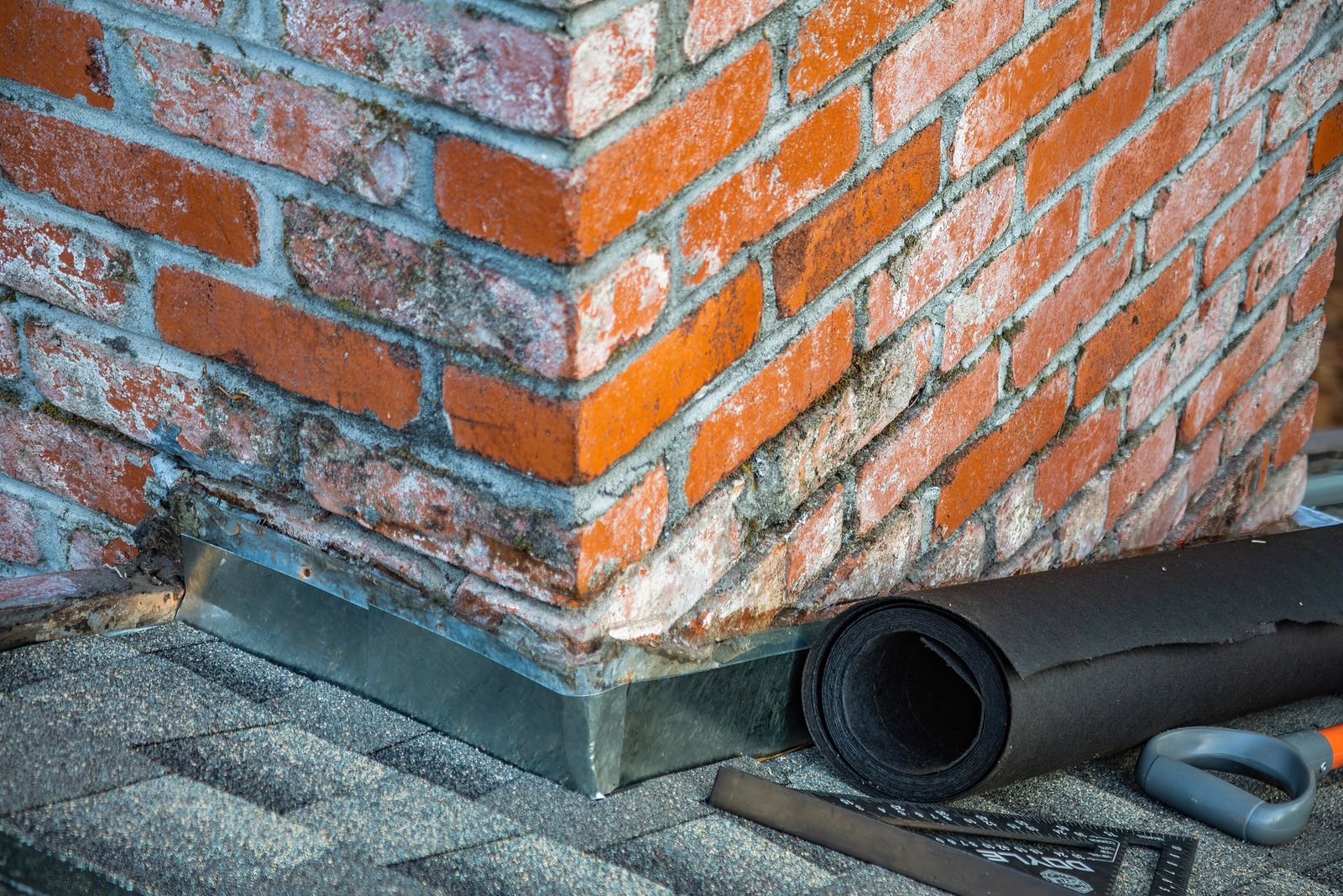 Metal flashing at the base of a brick chimney on an asphalt shingle roof